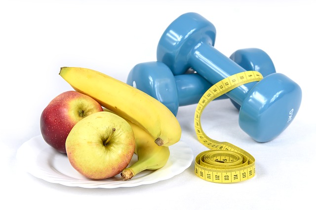 A simple recipe for a healthy body, healthy diet and exercise! Blue hand weights with a tape measure draped over them next to a plate of apples and bananas